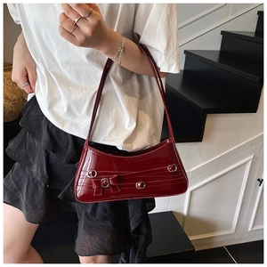 Close-up of deep red patent leather underarm bag with bow and silver buckle details