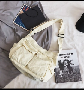 Detail of cream canvas crossbody bag featuring large front flap pockets and wide strap