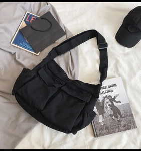 Detail of black canvas crossbody bag featuring large front flap pockets and wide strap