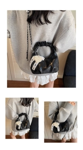 Detail of black pleated crossbody bag with embossed lettering and pearl bow charm