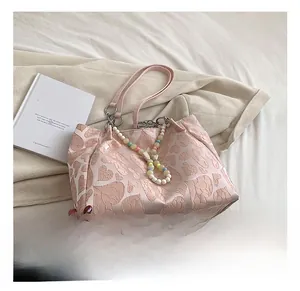 Detail of light pink heart textured tote bag with colorful beaded charm and satin finish