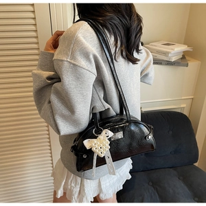 Détail du sac à bandoulière noir brillant avec nœud en perles et plaque logo argentée
