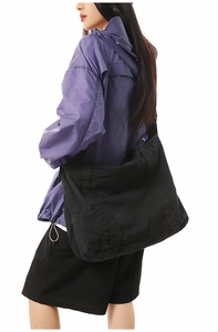 Detail of a large black canvas tote bag with front pocket shown on a model