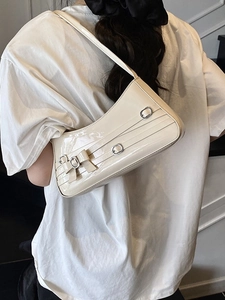 Cream patent leather baguette bag with bow and silver buckle shown on shoulder
