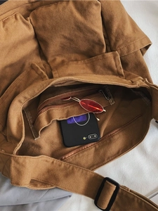 Brown canvas crossbody tote bag showing large capacity interior with phone and sunglasses