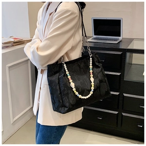 Detail of black embossed tote bag featuring a vibrant acrylic beaded decorative chain