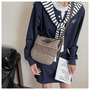 Detail of hand-woven hollow straw tote bag with brown leather strap and buckle