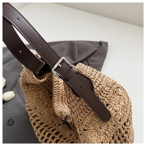 Detail of woven straw shoulder bag featuring brown leather strap and silver metal buckle