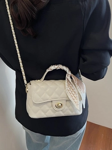 Quilted beige flap bag with gold hardware and silk scarf handle on black outfit