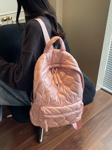 Pink quilted puffer backpack with wavy pattern and adjustable straps in a lifestyle setting