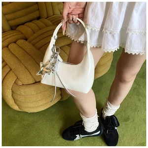Detail of white patent leather crescent bag featuring silver star charm and long metallic cord