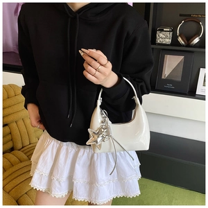 Detail of white patent leather crescent bag with silver star charm and metallic tassels