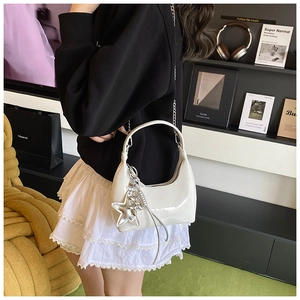 White glossy crescent moon bag with silver star charm and chain strap shown on shoulder