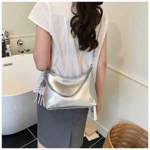 Detail of silver metallic tote bag with crinkled texture and woven fringe charm on shoulder