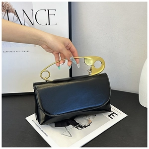 Détail du sac à bandoulière noir avec poignée en forme de grande épingle de sûreté dorée