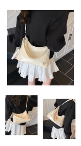 Close-up of ivory patent leather crescent bag featuring a metallic M logo and tassel detail