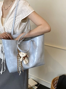 Sac cabas bleu clair à motif crocodile avec pendentif ours dans un intérieur lumineux
