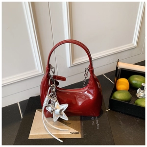 Detail of dark red patent leather bucket bag with silver star charm on a black book
