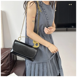 Détail du sac bandoulière en cuir noir avec poignée épingle dorée et bandoulière chaîne