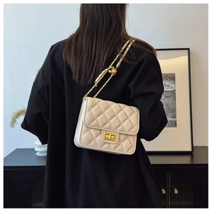 Détail d'un sac bandoulière matelassé beige avec fermoir doré et bandoulière chaîne cuir