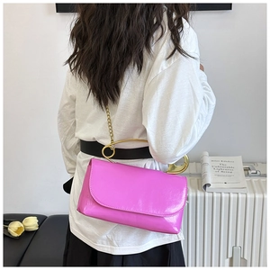 Détail d'un sac bandoulière rose vif avec une poignée métallique dorée en forme d'épingle