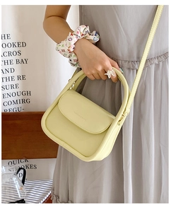 Detail of a pastel yellow mini flap bag with integrated handle and fashion text logo