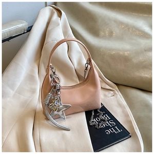 Detail of light pink patent leather hobo bag with silver chain and star charm on white suit