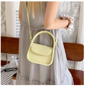 Close-up of a pale yellow faux leather crossbody bag featuring a curved top handle