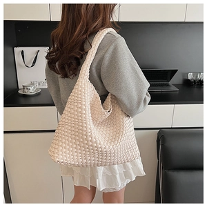 Detail of cream woven tote bag showing the texture and handle worn by a model