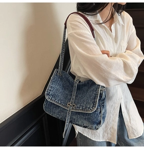 Detail of vintage washed denim tote bag with metal buckle and burgundy strap on model
