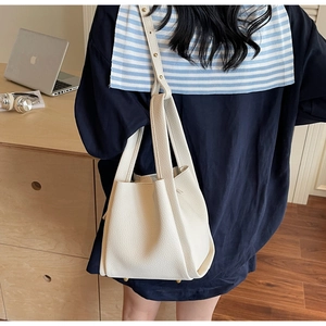 Close-up of a white lychee grain leather bucket bag with gold hardware on an office desk