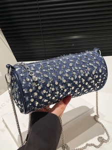 Sac cylindre en denim avec clous argentés et bandoulière chaîne tenu par un modèle
