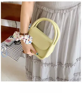 Close-up of light yellow semi-circular handbag with minimalist handle and flap closure