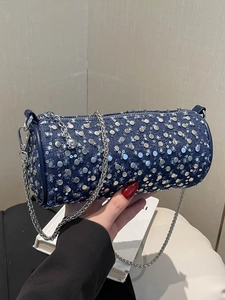 Sac cylindrique en jean bleu avec clous argentés et bandoulière chaîne à la main
