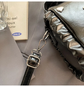 Close-up of black pleated bag with silver heart stud and metallic buckle detail