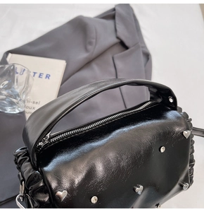 Macro detail of black glossy leather tote with heart studs and pleated ruffles