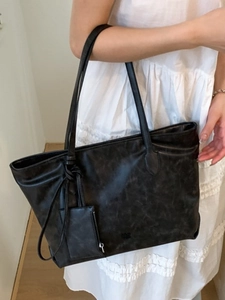 Minimalist black leather tote bag with shoulder straps and small matching zip pouch