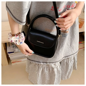 Detail of a black mini crossbody bag with gold lettering and sleek top handle design