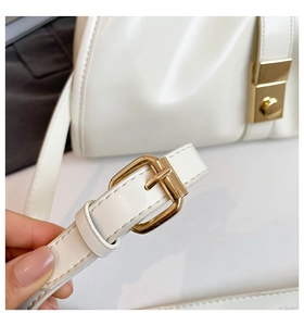 Close-up of golden buckle and clasp detail on elegant white patent leather handbag