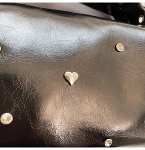 Close-up of black pebbled leather tote with silver heart stud and rhinestone details