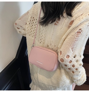 Close-up of pink lychee textured leather crossbody bag with zipper and logo detail