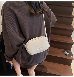 Close-up of cream textured leather crossbody bag with silver hardware on a model