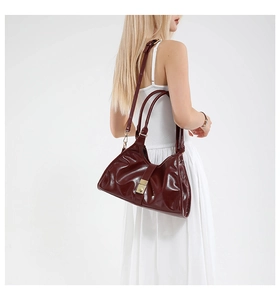 Detail of burgundy glossy leather handbag featuring golden clasp and adjustable shoulder strap