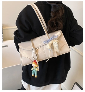 Detail of cream shoulder bag featuring a blue plaid bow and cute doll charm accessory