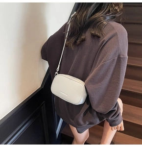 Close-up of cream litchi texture leather crossbody bag worn on shoulder over sweatshirt