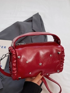 Red pleated barrel handbag with silver heart studs and ruffles shown in a casual setting