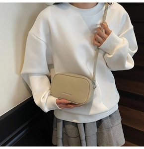 Detail of light beige pebbled leather camera bag with metallic logo and zipper closure