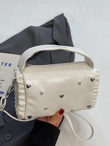 White pleated crossbody bag with heart-shaped crystal rivets and silver hardware on a blazer
