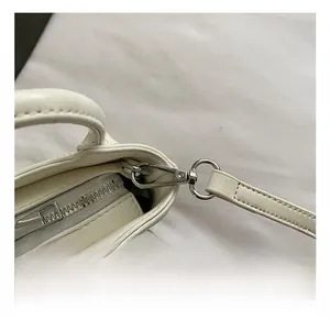 Close-up of premium silver metal hook and zipper on a white leather shoulder bag