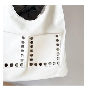Detail shot of white leather tote bag featuring metal hexagonal rivets and front pockets